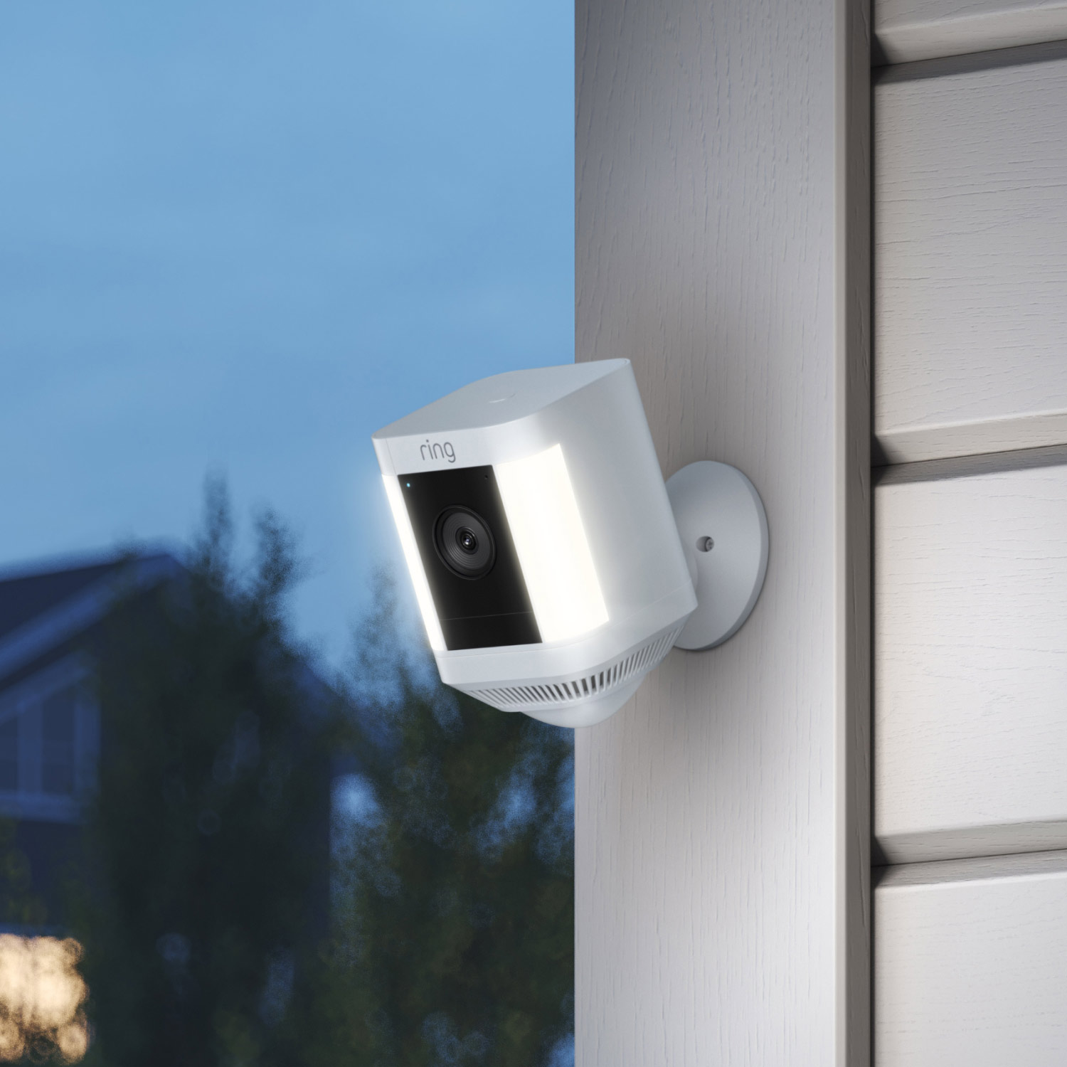 Front and Backyard Enhanced Kit (Spotlight Cam Plus Battery + Floodlight Cam Wired Plus) - White Ring Spotlight Cam Plus Battery mounted on exterior wall, lit up at dusk with trees and houses in the background.