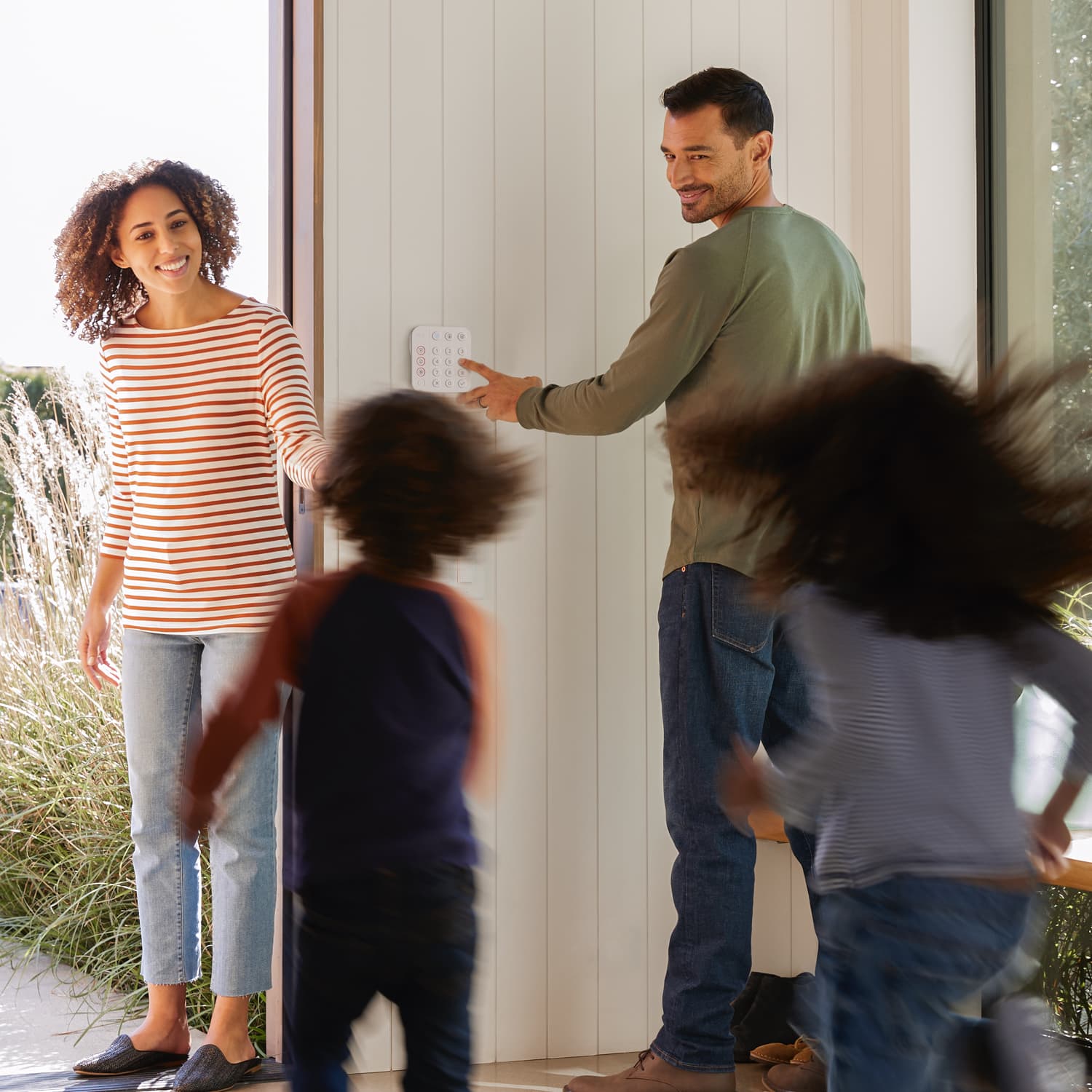 Alarm Security Kit, 10-Piece (for 2nd Generation) - Family exiting a home as a man uses a Ring Alarm Keypad on the wall, with two kids running toward a woman standing in the doorway.