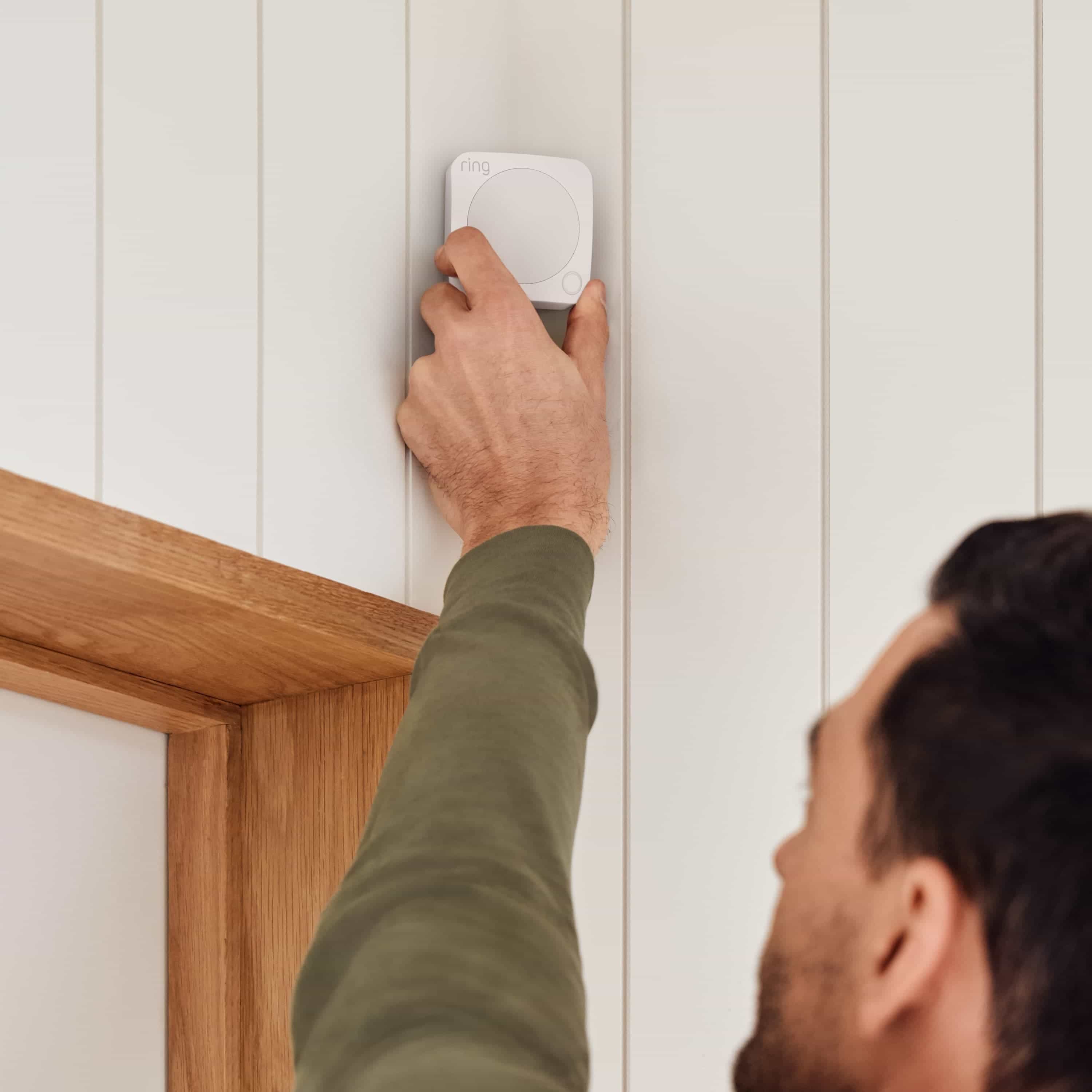 Alarm Security Kit, 10-Piece (for 2nd Generation) - Man installing a Ring Alarm Motion Detector on a wall above a doorway, showing easy setup of Ring Alarm Security Kit components for home protection.