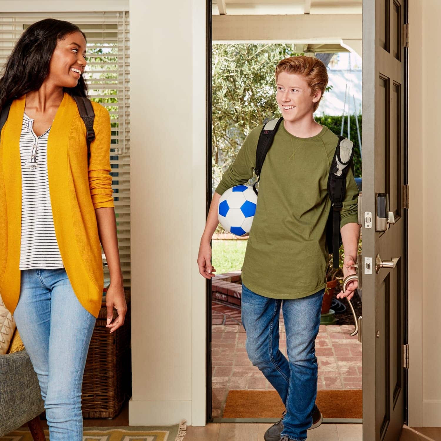 Schlage Encode Smart WiFi Deadbolt with Camelot Trim (for Works with Ring Video Doorbells and Cameras) - Teen girl and boy with soccer ball enters home through front door with Schlage Encode Smart Wi-Fi Deadbolt.