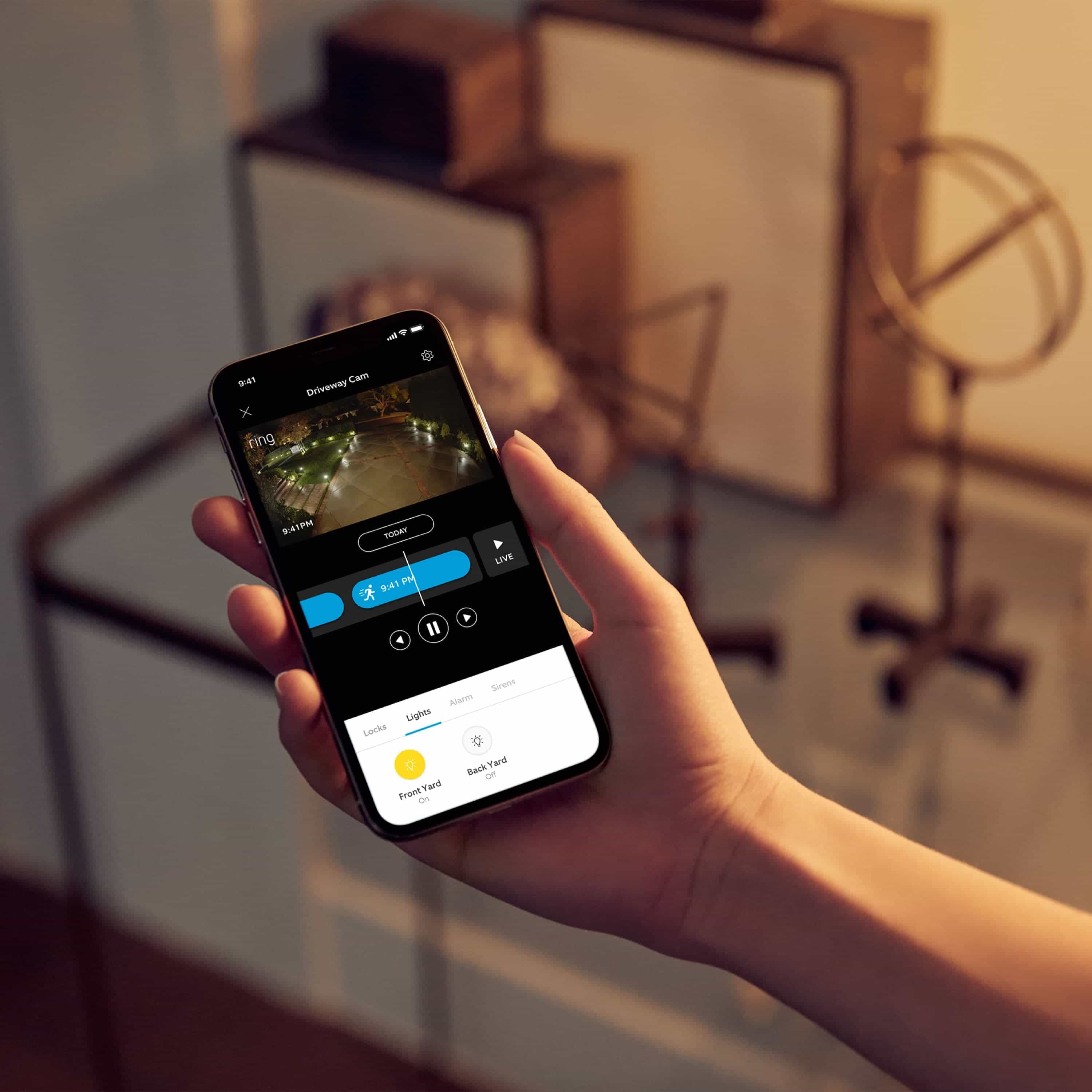 Smart Lighting Pathlight Battery - Hand holding smartphone showing Ring app live view and light controls for front and back yard smart lighting.