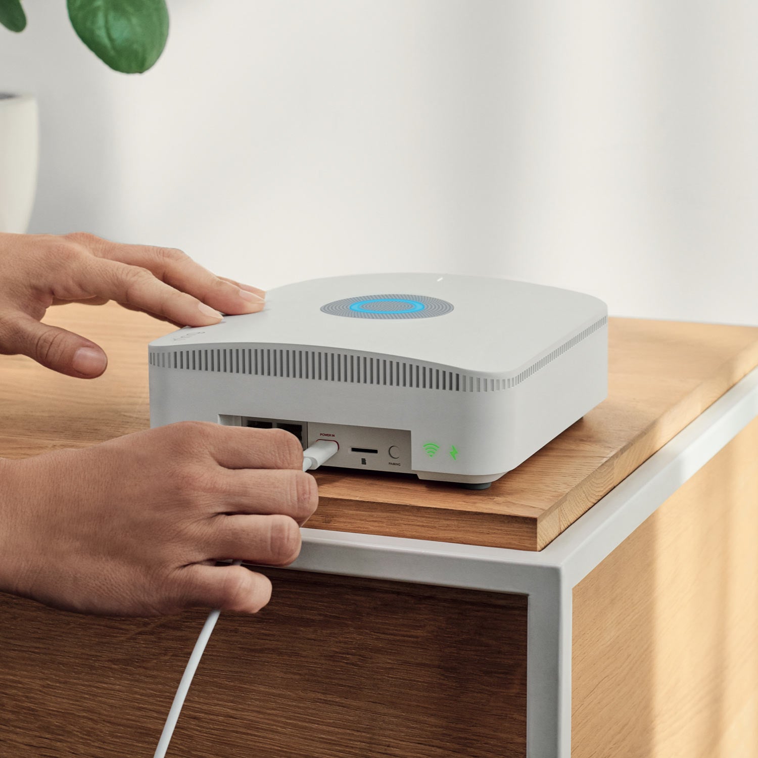 Alarm Pro Security Kit, 8-Piece (with built-in eero Wi-Fi 6 router) - Person plugging power cord into Ring Alarm Pro Base Station, with blue light glowing on top and rear ports visible.