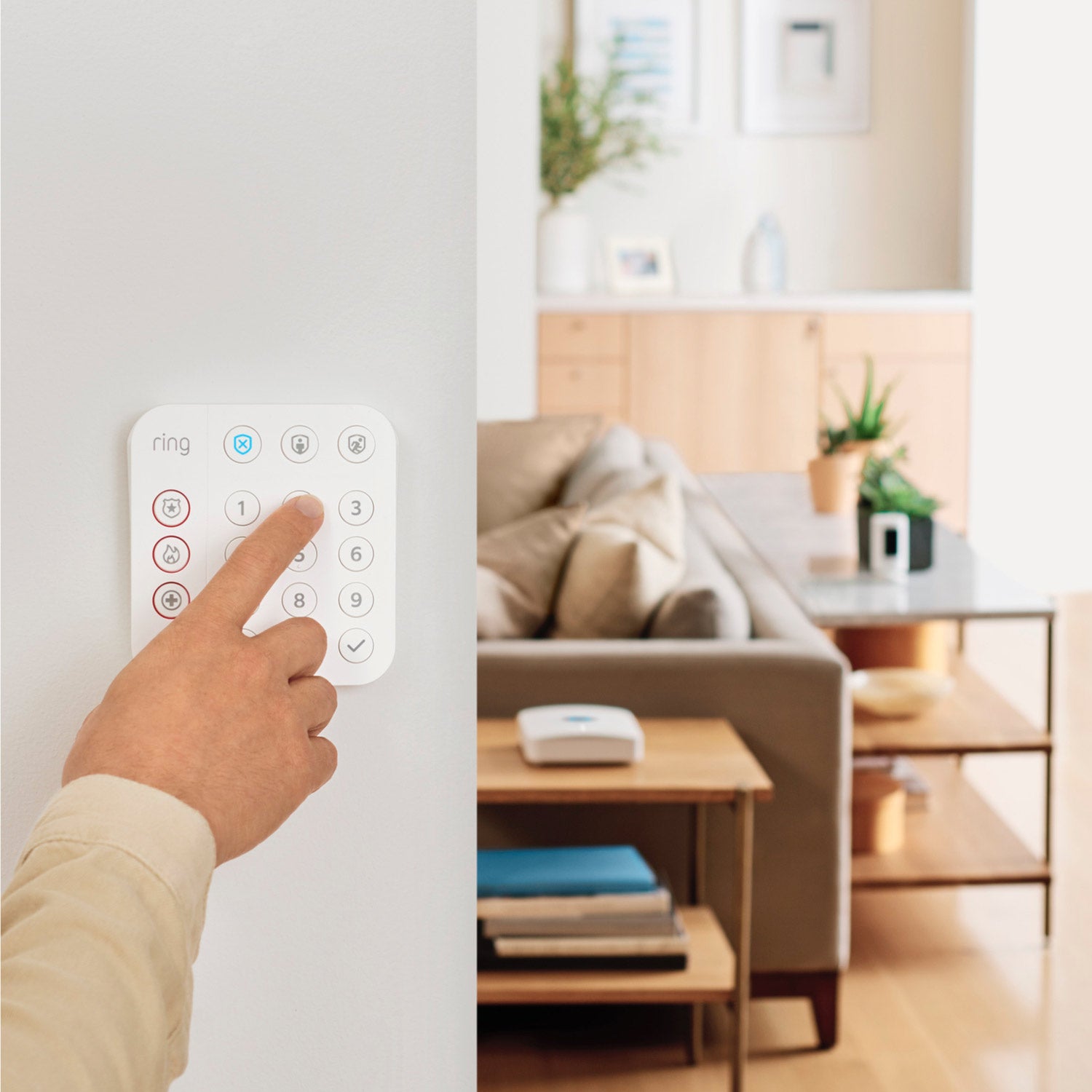 Alarm Pro Security Kit, 14-Piece (with built-in eero Wi-Fi 6 router) - Person pressing button on Ring Alarm Keypad mounted on wall, with a living room and Ring Alarm Pro Base Station visible.