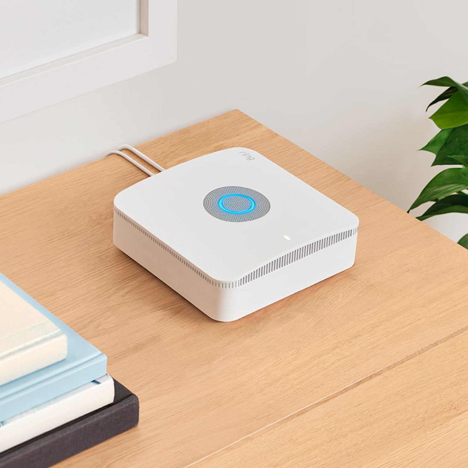 Alarm Pro Security Kit, 14-Piece (with built-in eero Wi-Fi 6 router) - Ring Alarm Pro Base Station with glowing blue light and power cables extending from the back, shown on a wooden table.