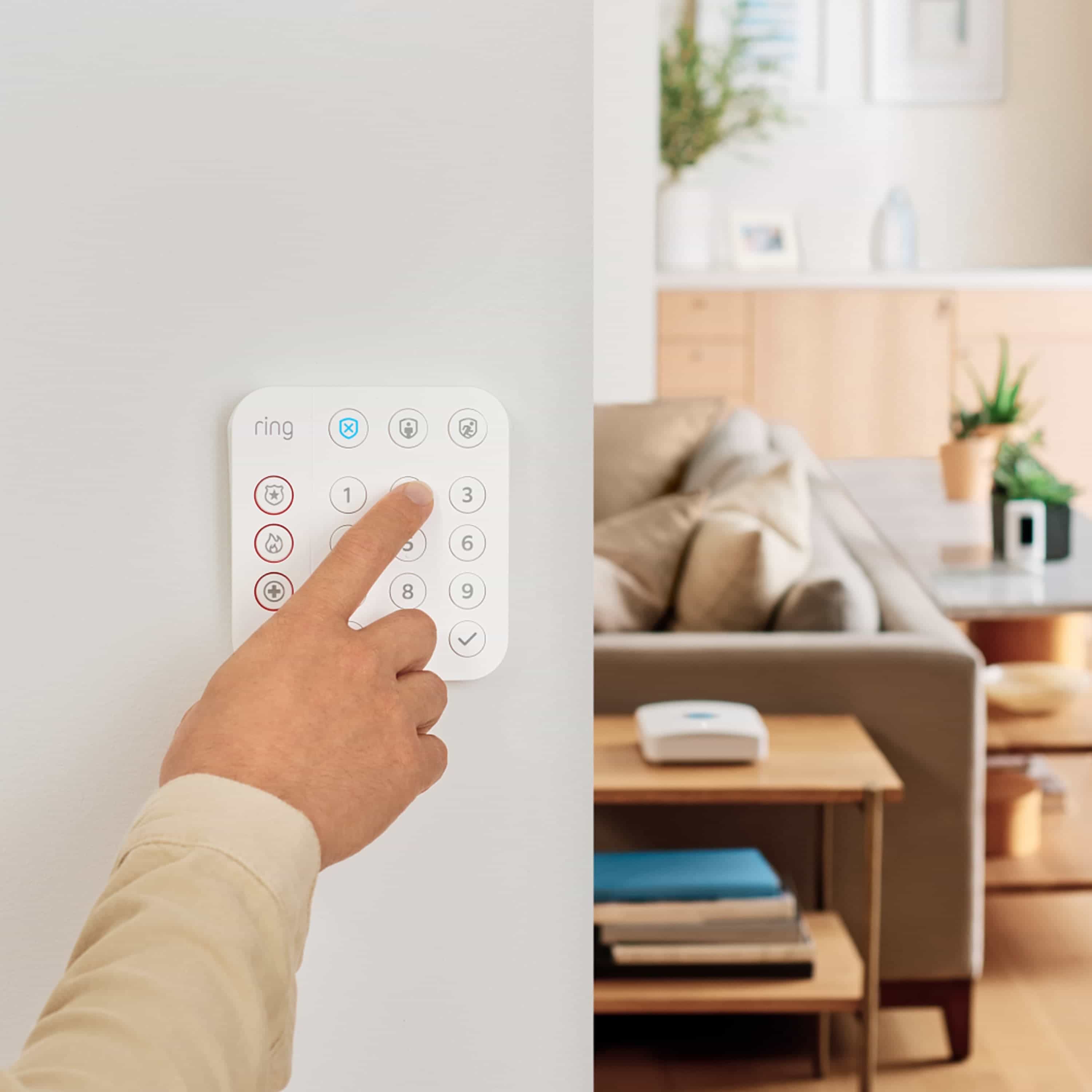 Alarm Security Kit, 14-Piece (2nd Generation) - Person pressing a button on a white Ring Alarm Keypad mounted on a wall, with a living room visible in background.