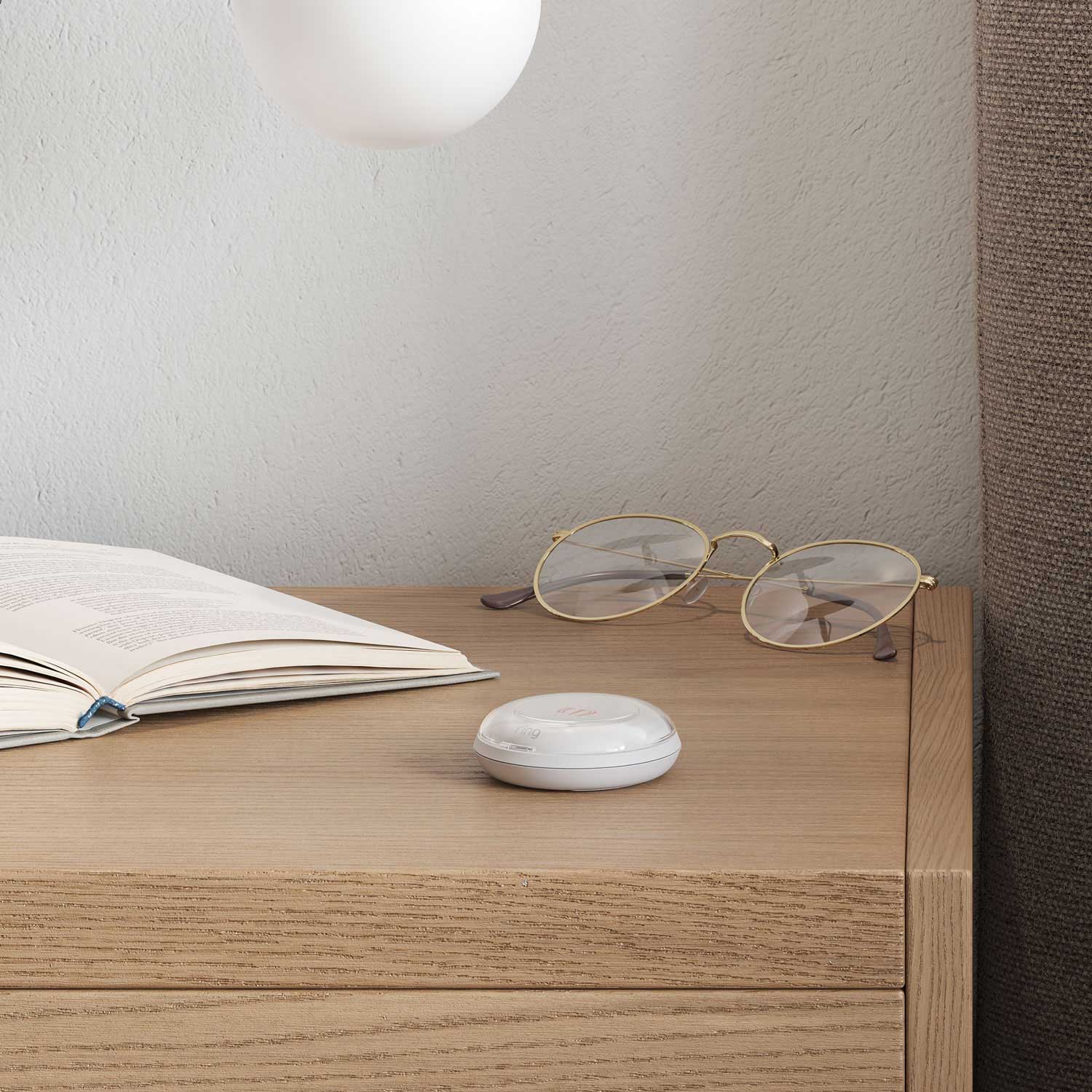2-Pack Panic Button (2nd Gen) - Ring Panic Button on a bedside table next to an open book and eyeglasses, ready for emergency use.