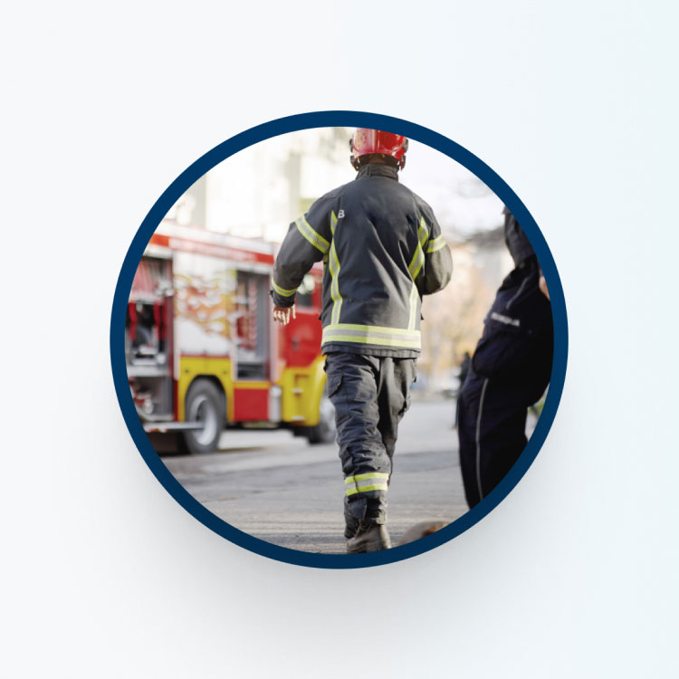 A firefighter in protective gear and a red helmet walks toward a red and yellow fire truck.