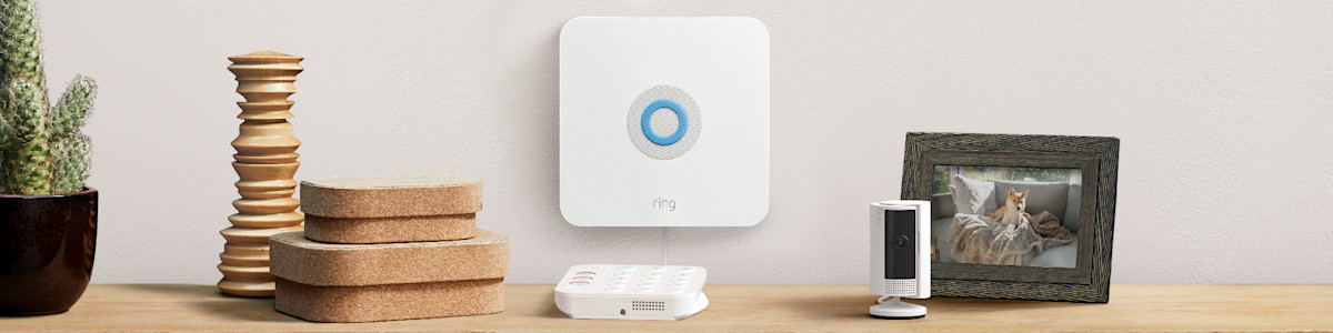 Ring Alarm Base Station, a white Ring security camera, and a Ring Alarm Keypad on a wooden surface