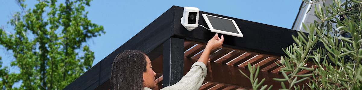 A person installing an outdoor Ring security camera and solar panel on a patio pergola