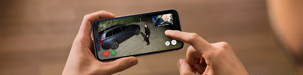 Hands holding phone displaying Ring security camera feed of car and person on driveway