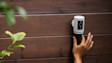 Hand installing a Ring Quick Release battery in a Ring security camera on a wooden fence